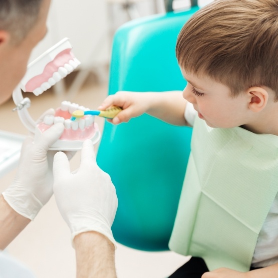 Child brushing model teeth held by children's dentist in Centennial