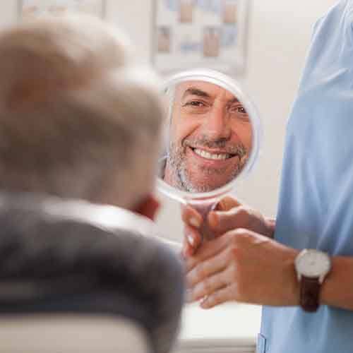 Man smiling while looking at reflection in handheld mirror